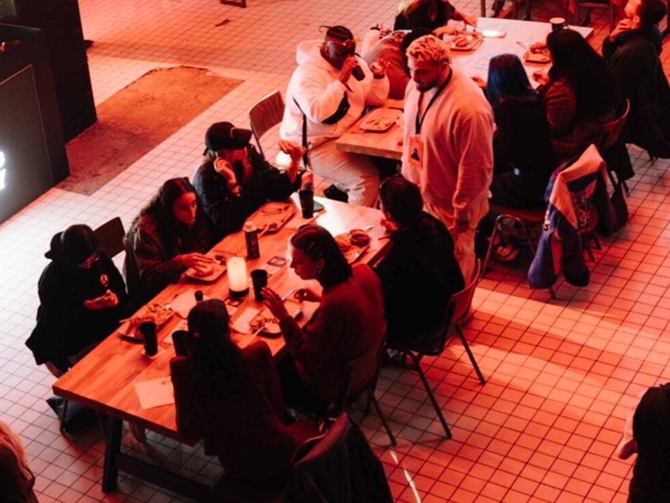 Deelnemers eten samen aan lange tafels, van bovenaf gezien
